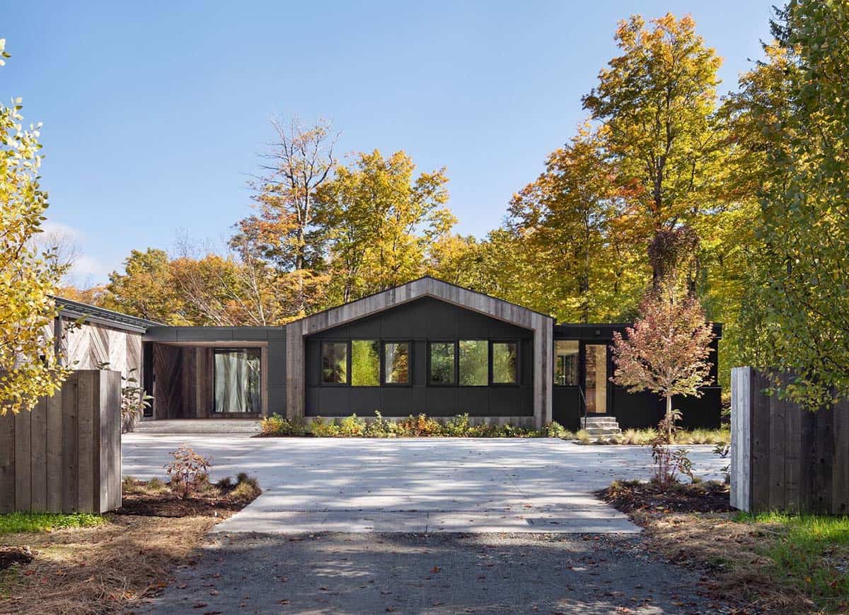 Front facade of renovated mountain house with dark cladding, gabled roof, and reclaimed wood accents in fall foliage