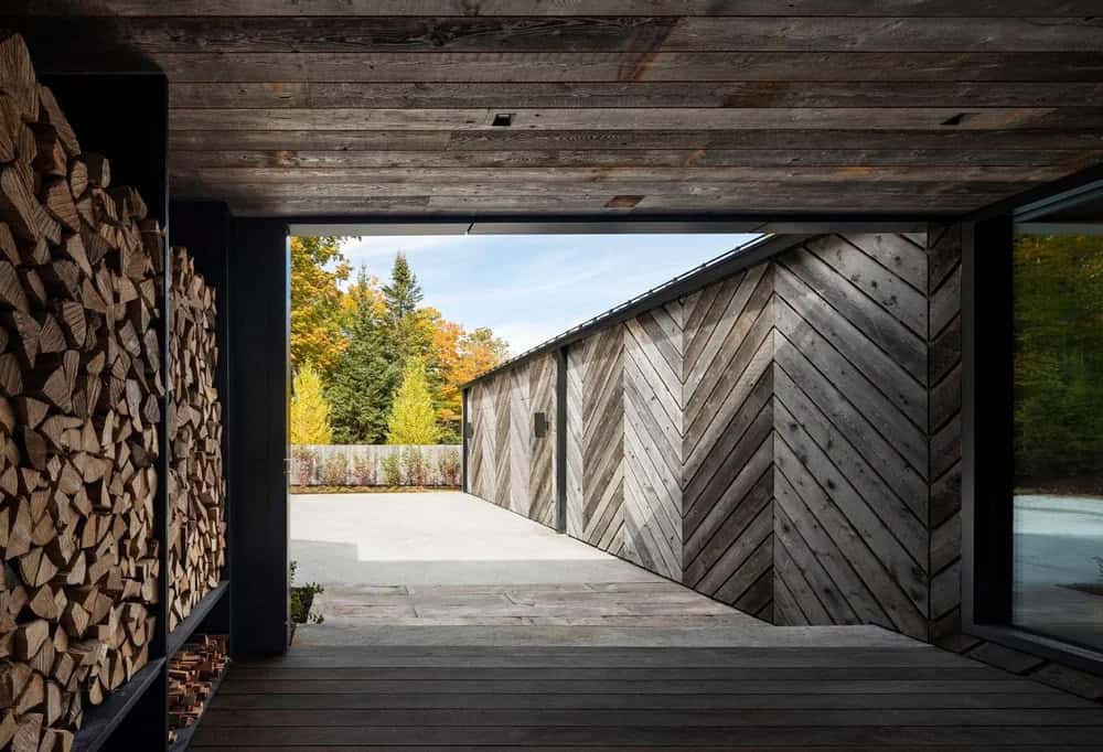 Covered entryway passageway with reclaimed wood ceiling, stacked firewood wall, and chevron-patterned exterior siding
