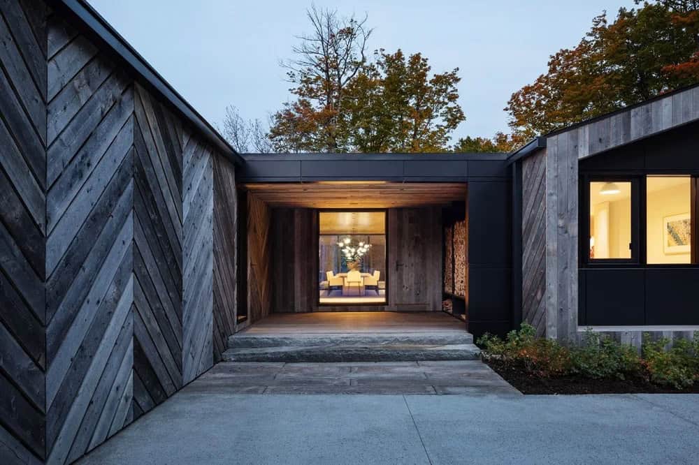 Dusk view of home's open breezeway entrance with warm interior dining room visible through glass