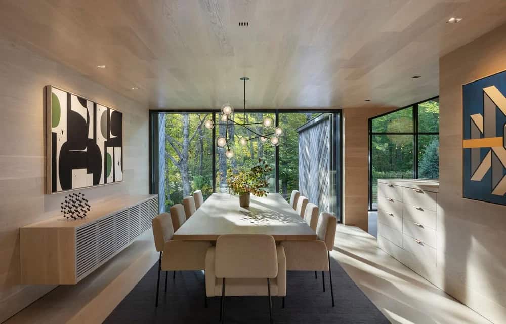 Modern dining room with white oak ceiling, long white table, globe chandelier, and floor-to-ceiling forest views