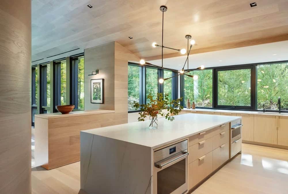 Contemporary kitchen with white marble island, light wood cabinetry, sputnik pendant lights, and wraparound forest windows