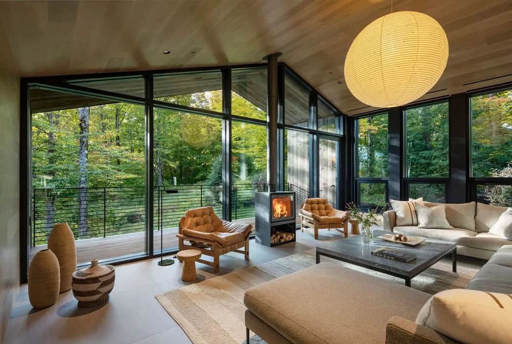 Living room with floor-to-ceiling glass walls, freestanding wood stove, leather lounge chairs, and paper lantern pendant