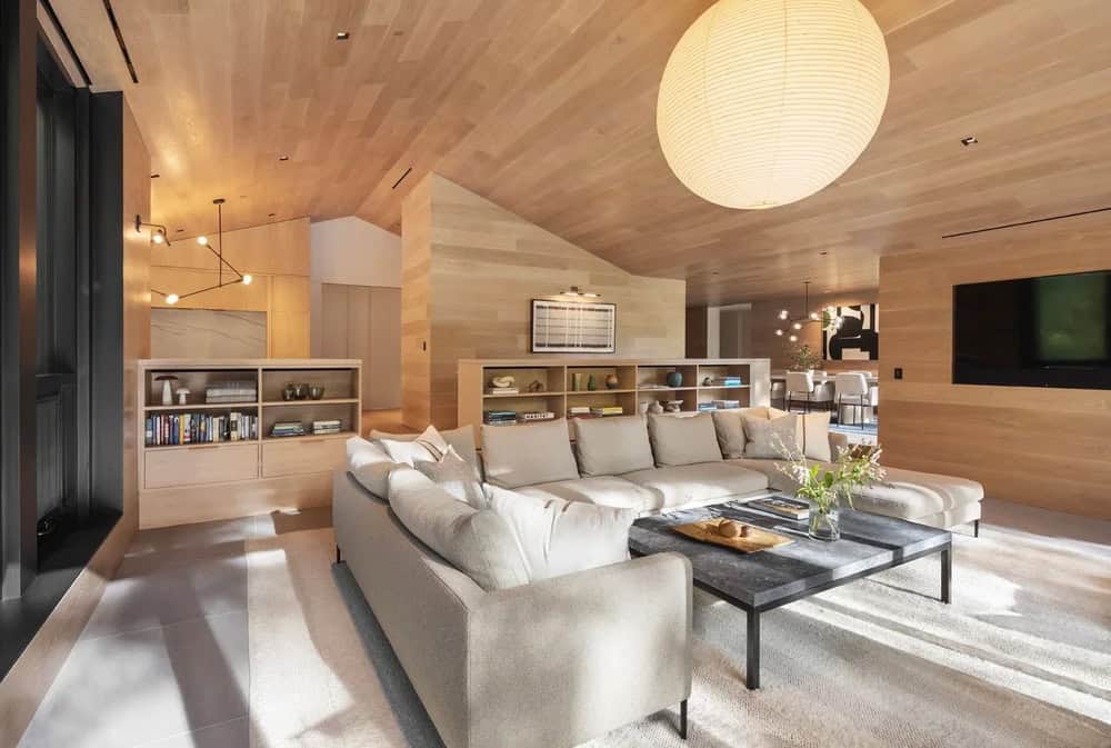 Open-plan living area with vaulted wood ceiling, large sectional sofa, globe pendant light, and views into kitchen