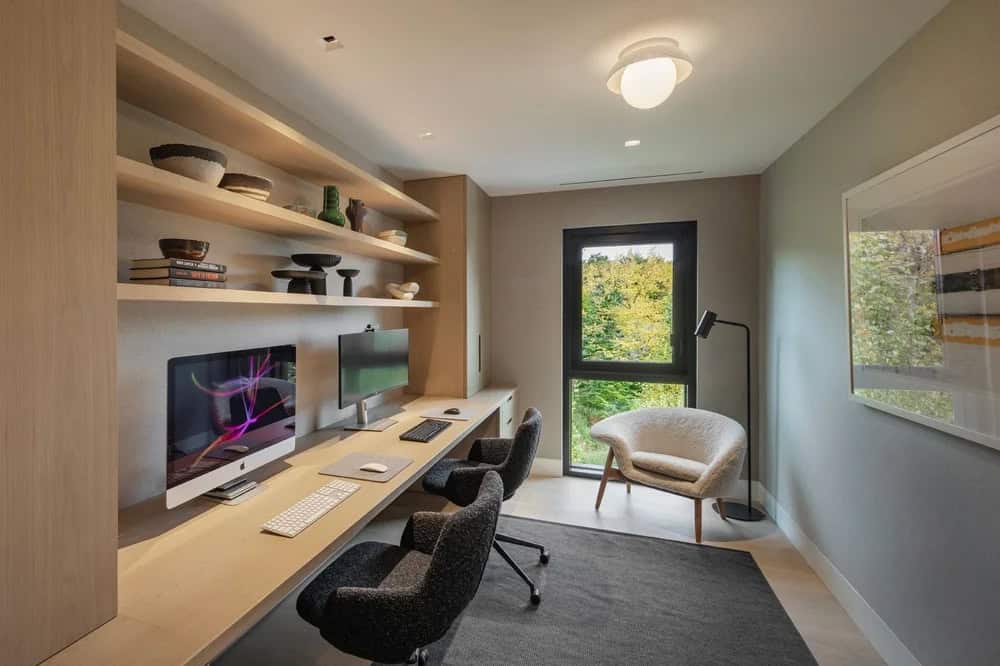 Home office with built-in wood desk, floating shelves, two iMacs, and garden-view window