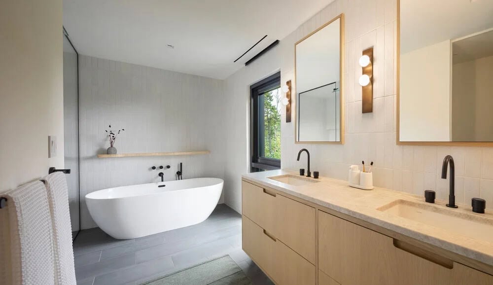 Primary en-suite bathroom with freestanding soaking tub, double oak vanity, black fixtures, and gold-framed mirrors