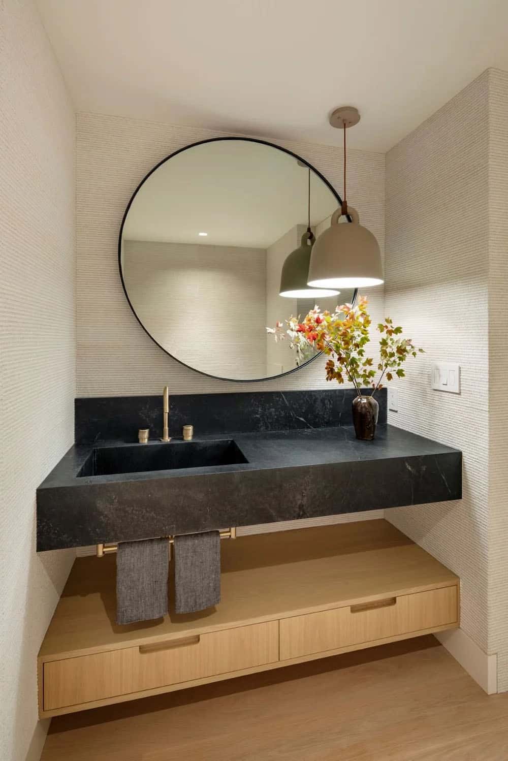 Bathroom vanity with floating black stone sink, round mirror, pendant light, and light oak storage drawers