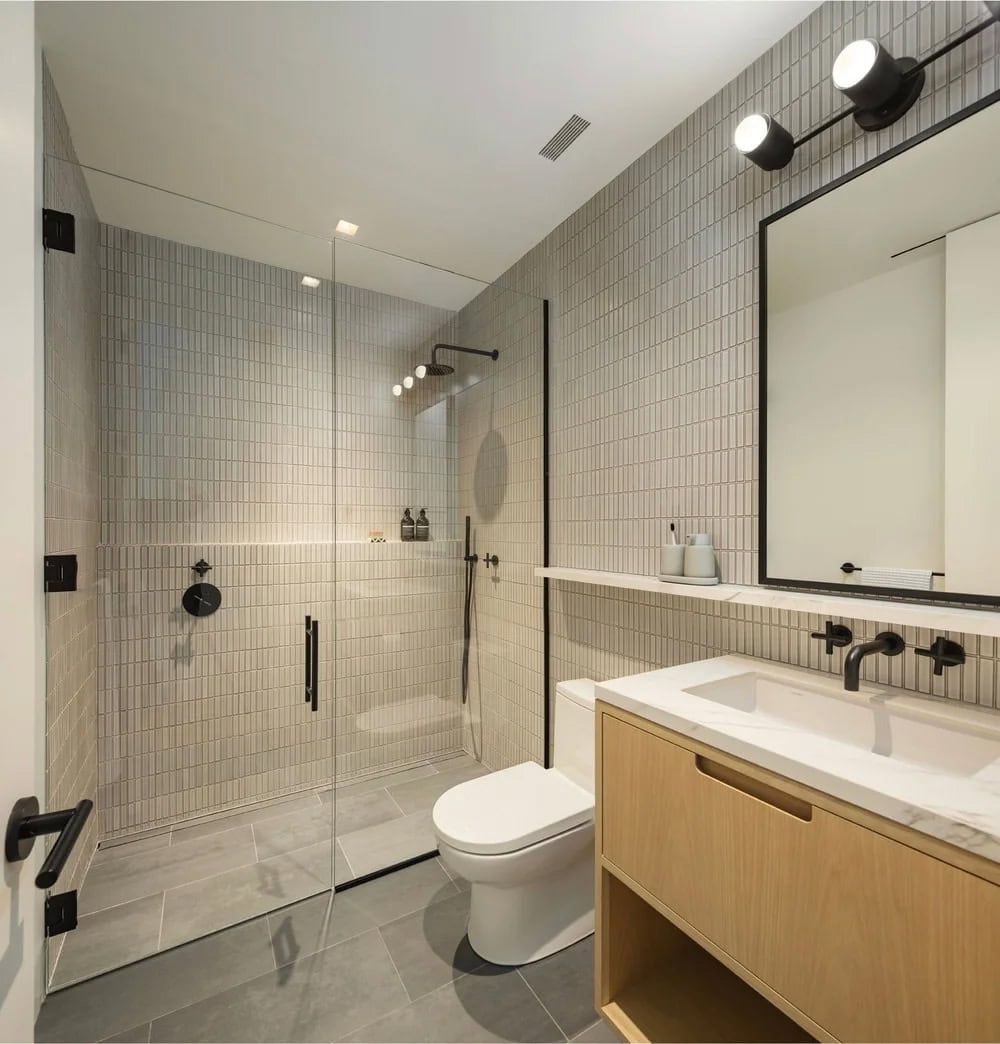 Modern bathroom with vertical white tile, frameless glass shower, floating oak vanity, and black fixtures