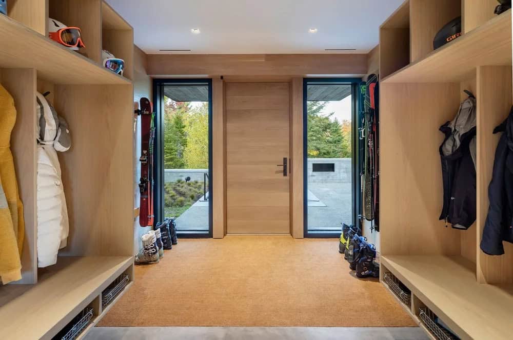 Ski mudroom with built-in oak cubbies, benches, ski and snowboard storage, helmets, and wood pivot front door