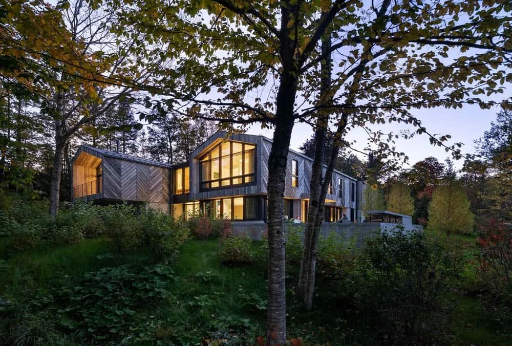Dusk exterior view of mountain home with glowing interior lights, chevron wood cladding, and tall gabled windows