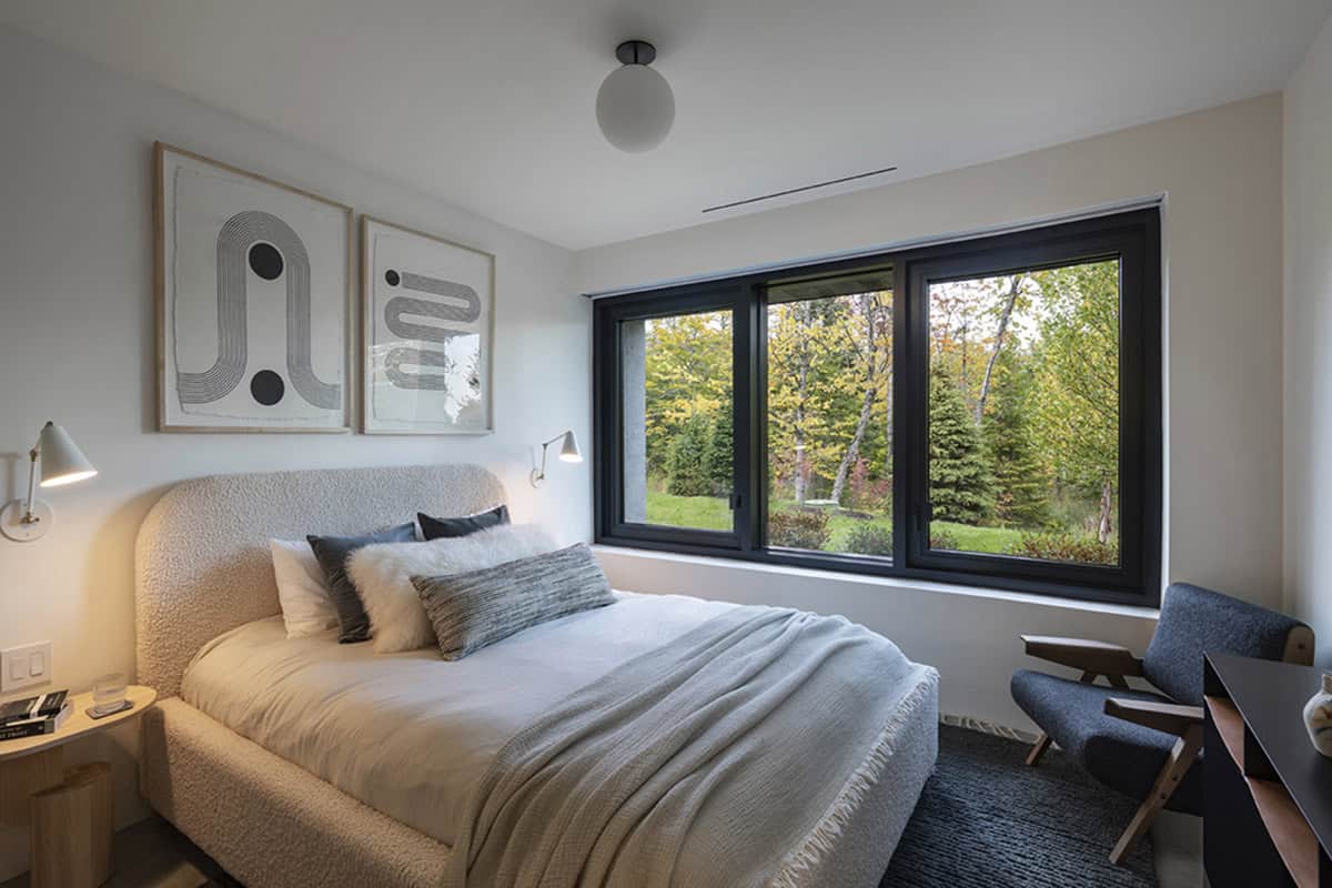 Guest bedroom with boucl&eacute; arched headboard, wall-mounted reading lamps, abstract artwork, and wide forest-view window