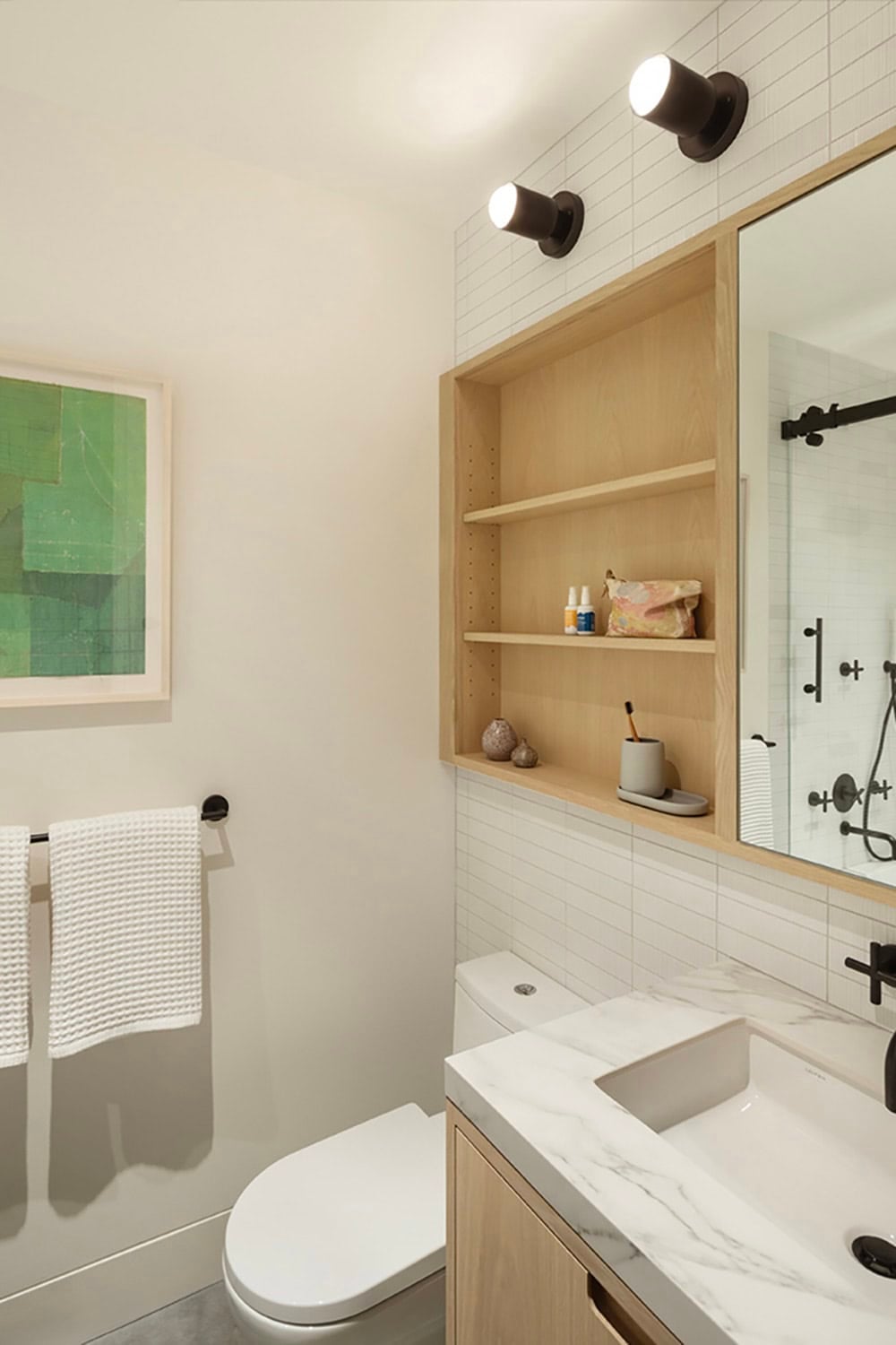 Guest bathroom with white stacked tile, built-in oak shelving niche, marble vanity top, and black fixtures