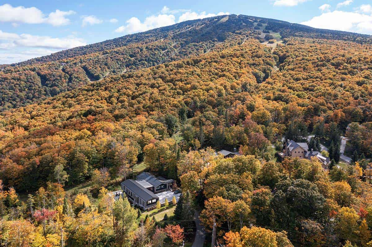 Wide aerial drone view of ski house nestled at the base of a Vermont mountain amid peak fall foliage