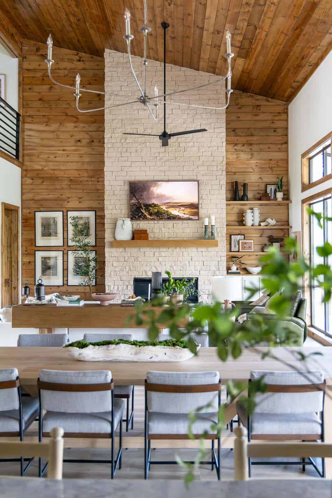 Open living area with vaulted wood ceiling, stone fireplace, chandelier, and dining table