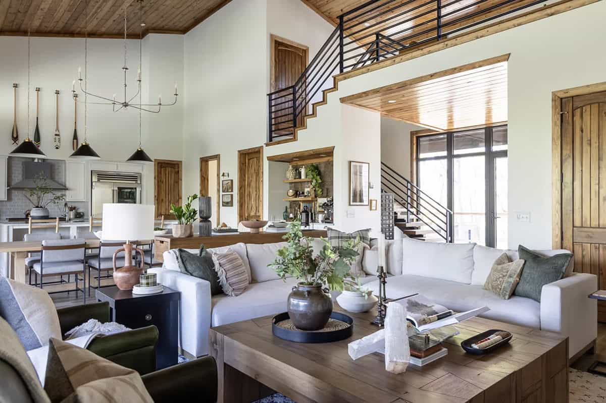 Open-concept living room with white sofas, wood coffee table, and staircase with black metal railing
