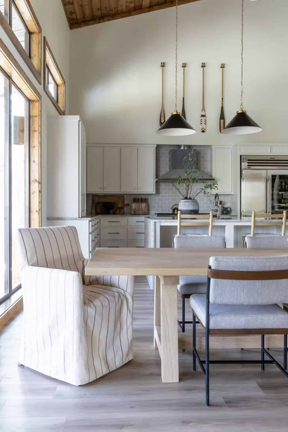 Dining area with light wood table, mixed chairs, black pendant lights, and white kitchen beyond