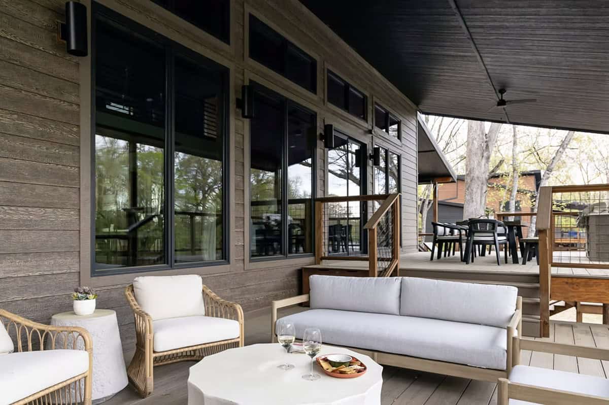 Covered deck with rattan and upholstered seating, dark ceiling, and outdoor dining area