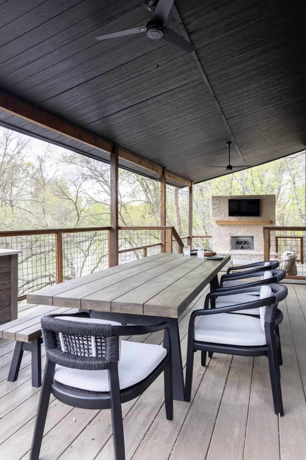 Covered outdoor dining area with gray wood table, black rope chairs, and stone fireplace