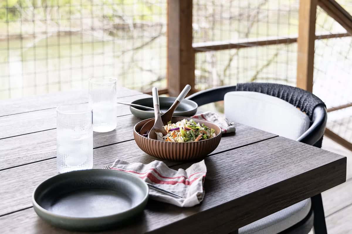 Outdoor dining table set with stoneware plates, a salad bowl, and water glasses