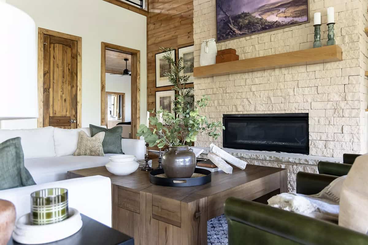 Living room seating area with stone fireplace, wood shiplap wall, and olive tree centerpiece