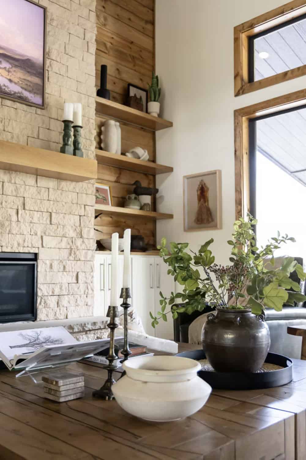 Coffee table vignette with brass candlesticks, ceramic bowls, and dark pottery vessel