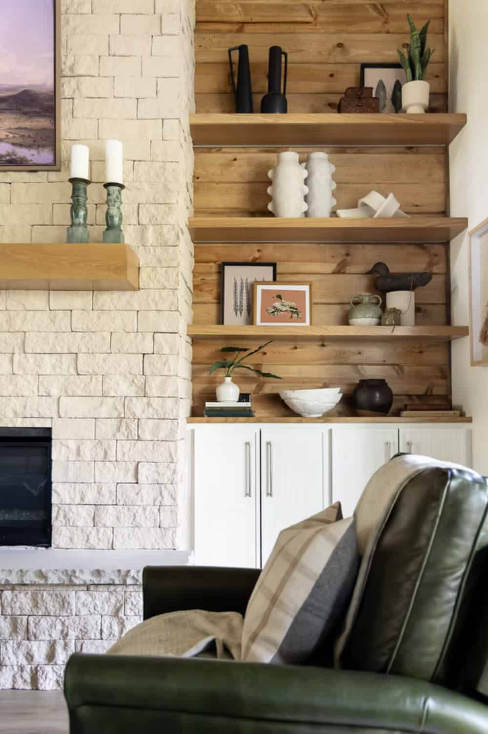 Stone fireplace with wood mantle, flanking shelves styled with ceramics and nature-themed art