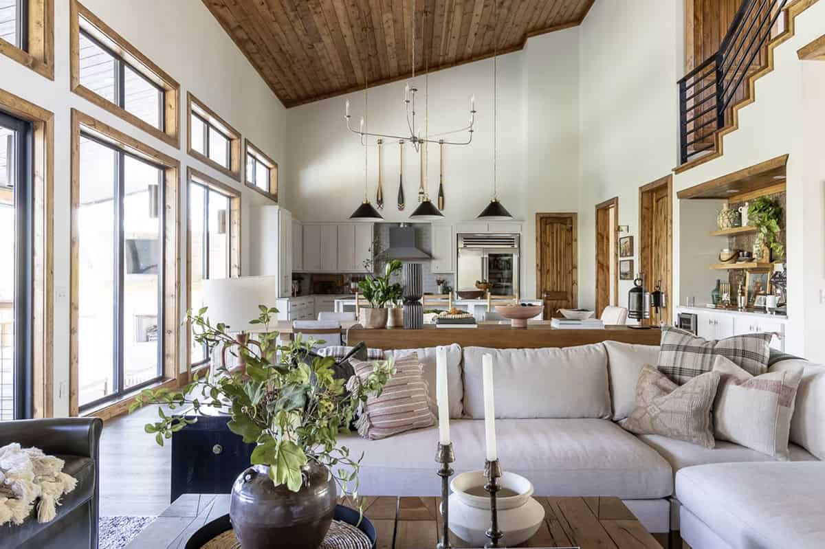 Open living room with vaulted wood ceiling, white sectional sofa, oar pendant lights, and kitchen beyond