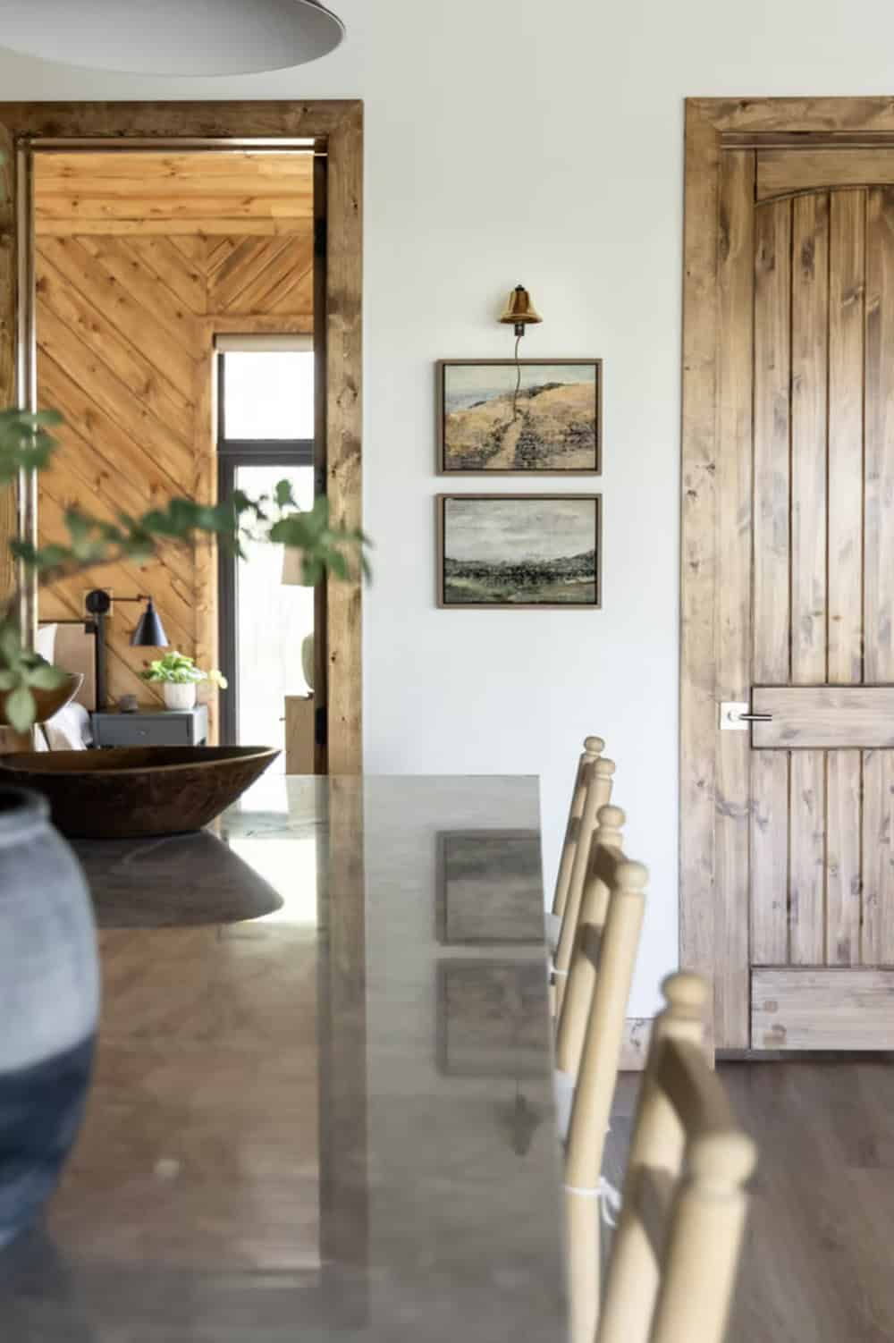 Polished concrete dining table with wood chairs, two landscape paintings, and rustic knotty wood door
