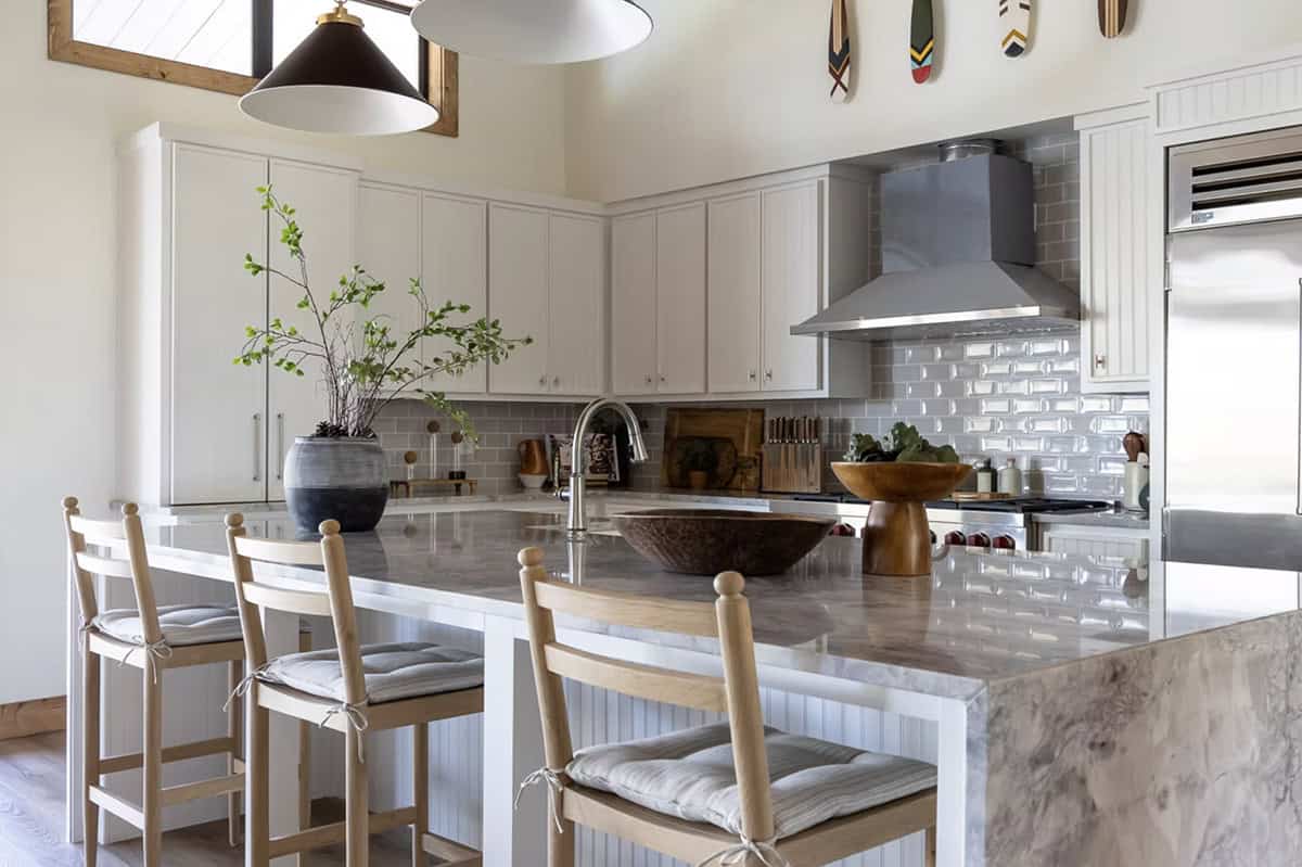 White kitchen with marble island, wood bar stools, gray subway tile backsplash, and black pendant lights