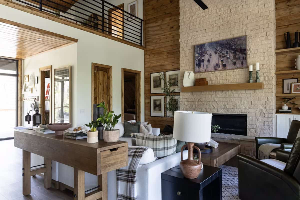 Living room with stone fireplace, linen sofa, plaid throw, wood console table, and loft railing above