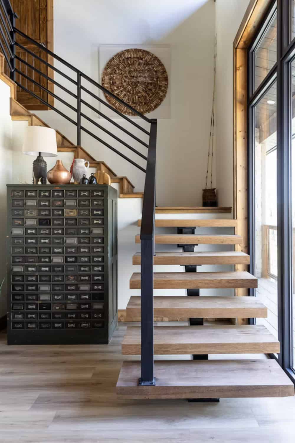 Open-riser staircase with black metal railing, vintage multi-drawer cabinet, and round woven wall art