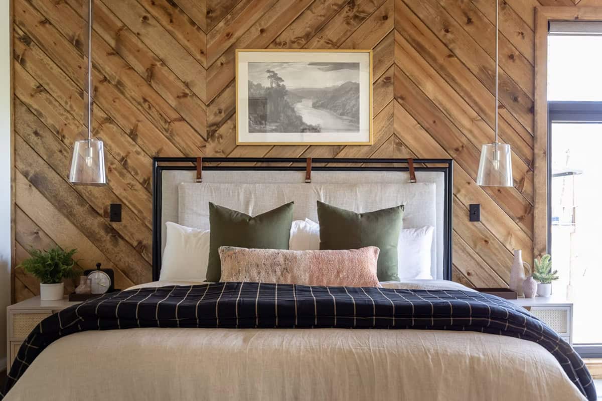 Close-up of main bed with chevron wood wall, linen headboard, green velvet pillows, and glass pendants