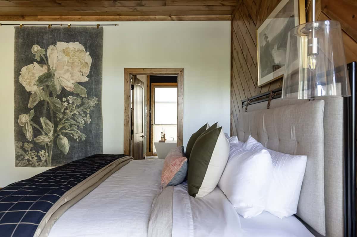 Guest bedroom with linen headboard, large floral tapestry wall hanging, and view to ensuite bathroom