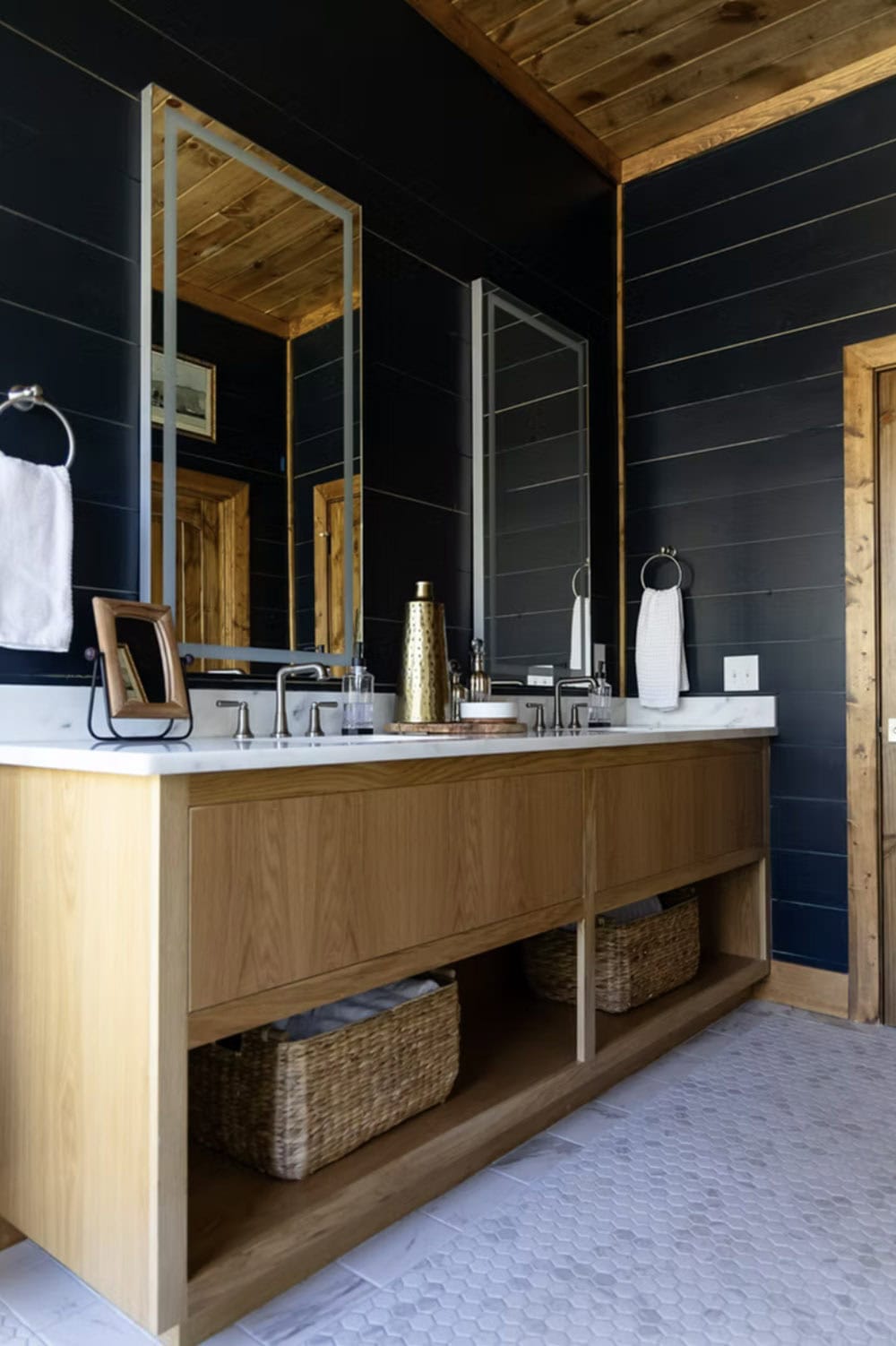 Main bathroom with black shiplap walls, wood vanity, marble countertop, wicker baskets, and hexagon tile floor