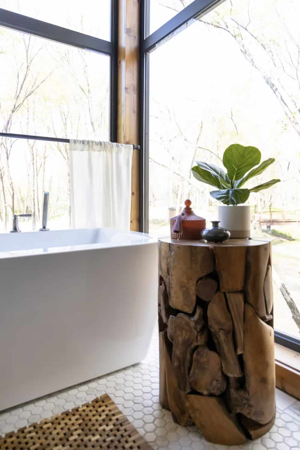 Freestanding soaking tub beside a driftwood side table topped with a fiddle leaf fig plant