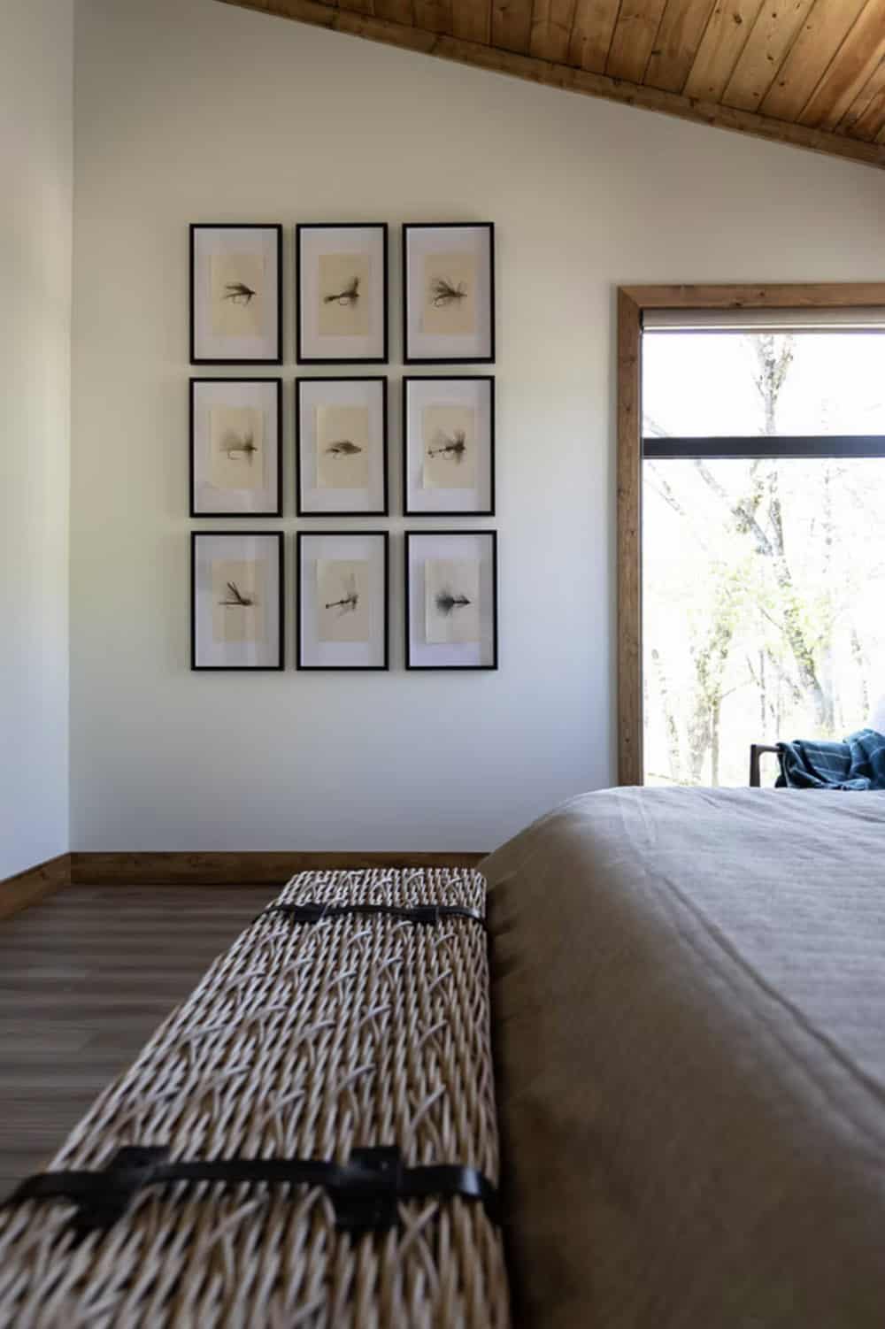 Wicker storage bench at foot of bed with 3x3 grid of framed fly fishing illustrations on wall