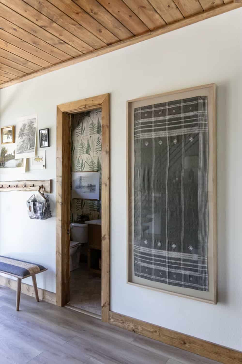 Hallway with framed textile art, powder room with botanical fern wallpaper, and wood-trimmed doorways