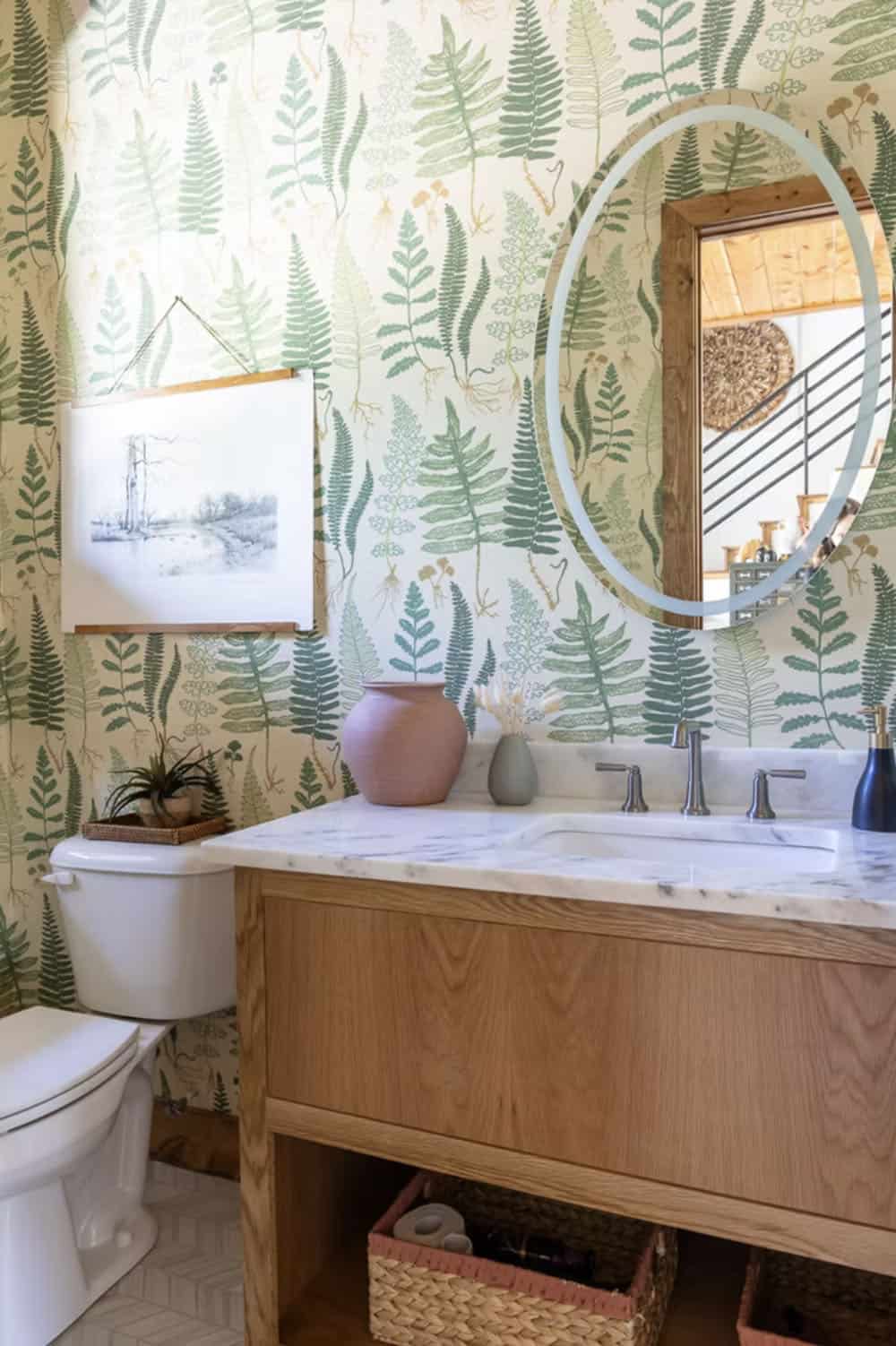 Powder room with green fern botanical wallpaper, wood vanity, marble countertop, oval mirror, and pink vase