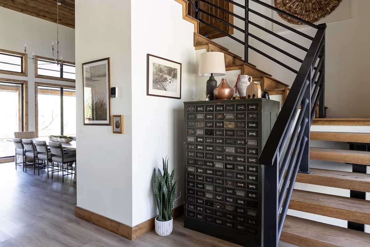 Wide view of staircase hall with vintage cabinet, snake plant, framed landscape art, and dining room beyond