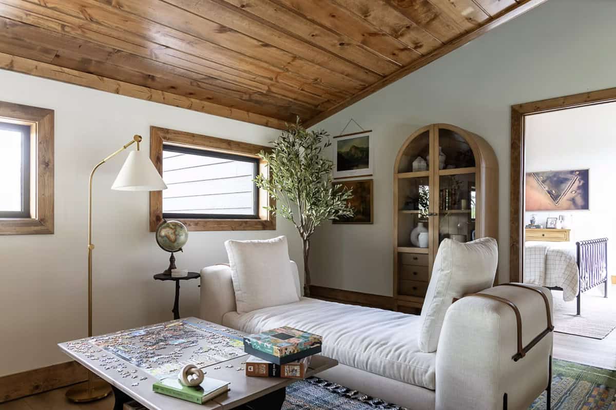 Upstairs loft sitting room with white chaise, arched wood cabinet, olive tree, globe, and puzzle table