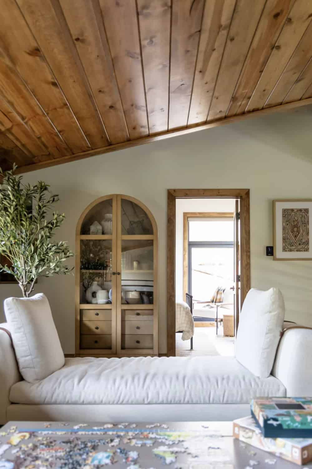 Loft sitting area with arched wood display cabinet, white chaise lounges, and in-progress puzzle on coffee table