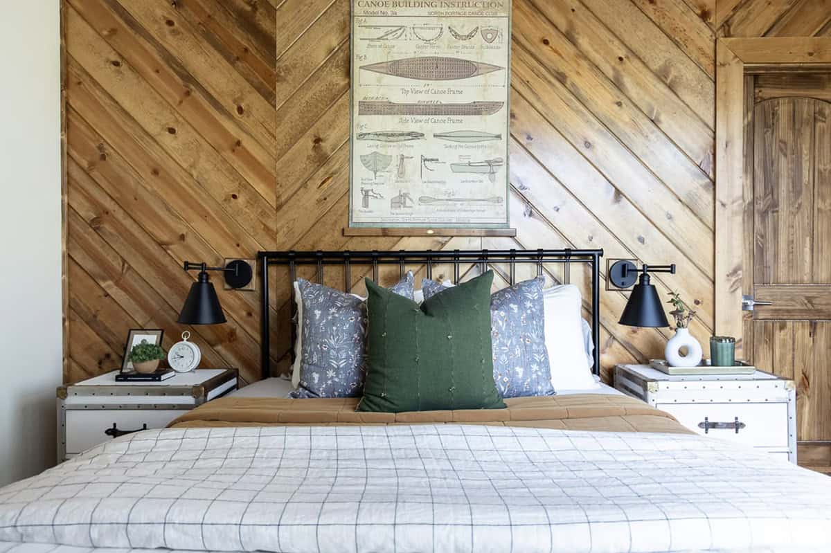 Iron bed headboard close-up with green and floral pillows, trunk nightstands, and canoe blueprint above