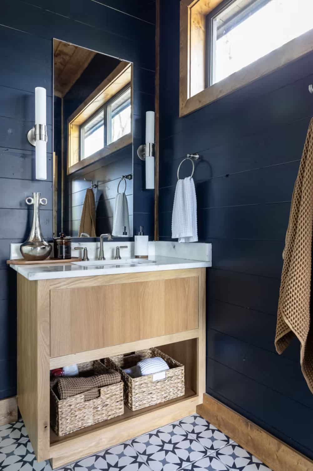 Ensuite bathroom with dark navy shiplap, wood vanity, marble countertop, geometric tile floor, and tube sconces