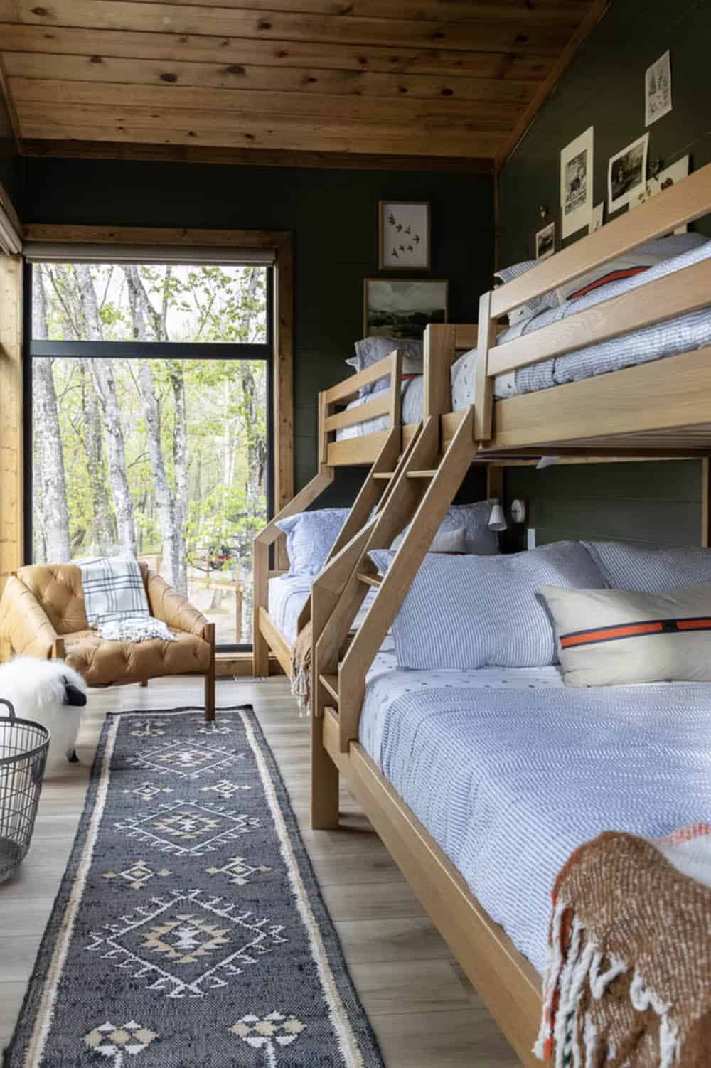 Bunk room with dark green walls, double bunk beds, tribal runner rug, and tufted leather chair by window