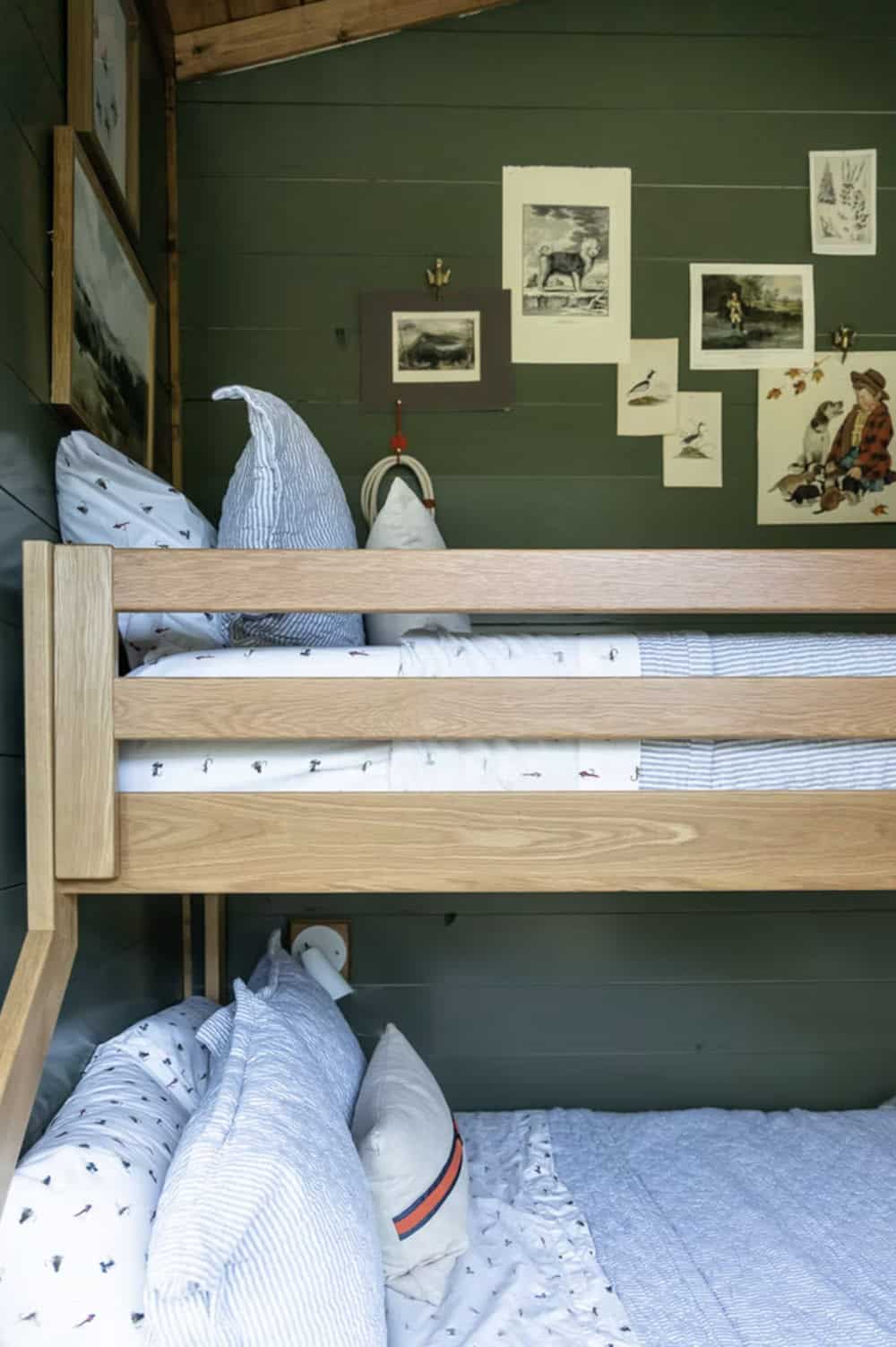 Close-up of wood bunk beds against dark green shiplap wall with vintage nature prints pinned above
