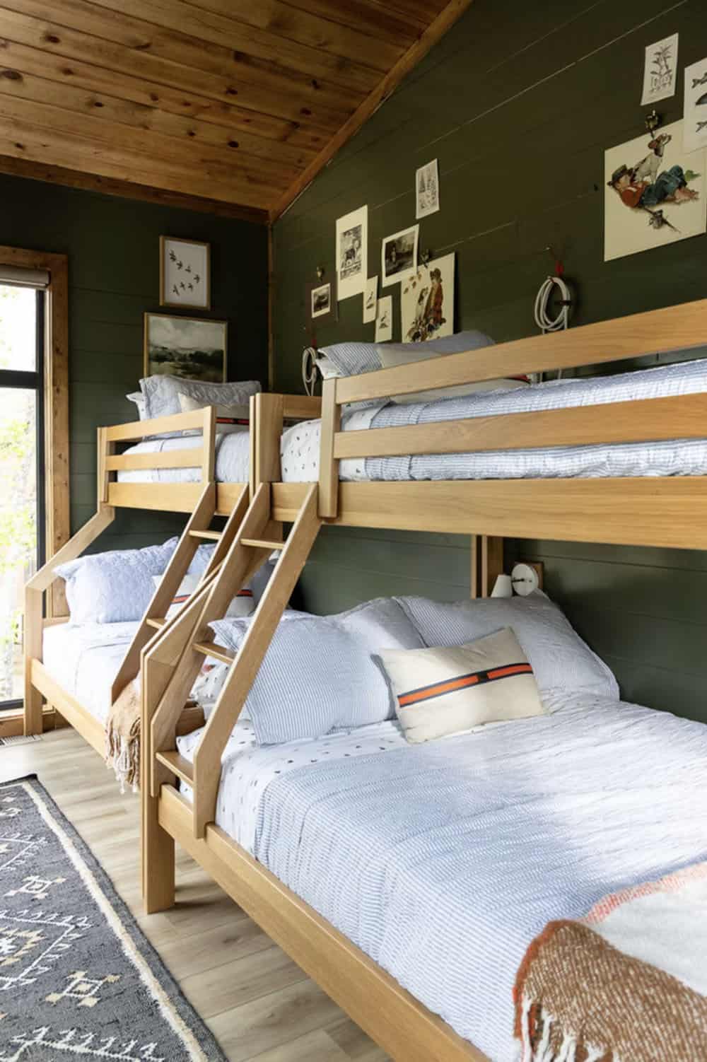Green shiplap bunk room with two sets of wood bunk beds, tribal runner rug, and nature art collage