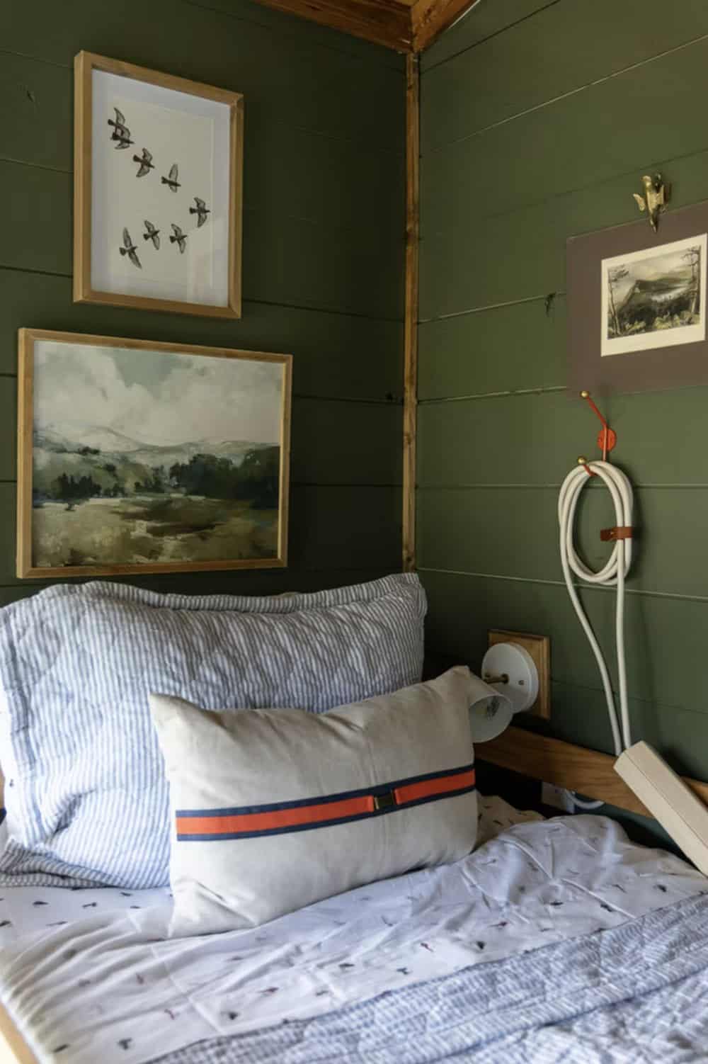 Lower bunk detail with seersucker bedding, linen pillow, bird art, and landscape painting on green wall