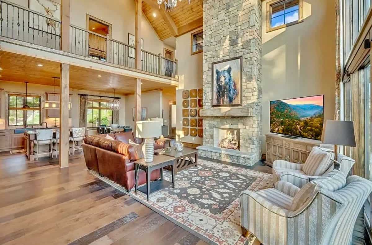 Open-plan living area with two-story stone fireplace, loft balcony, and wood ceiling