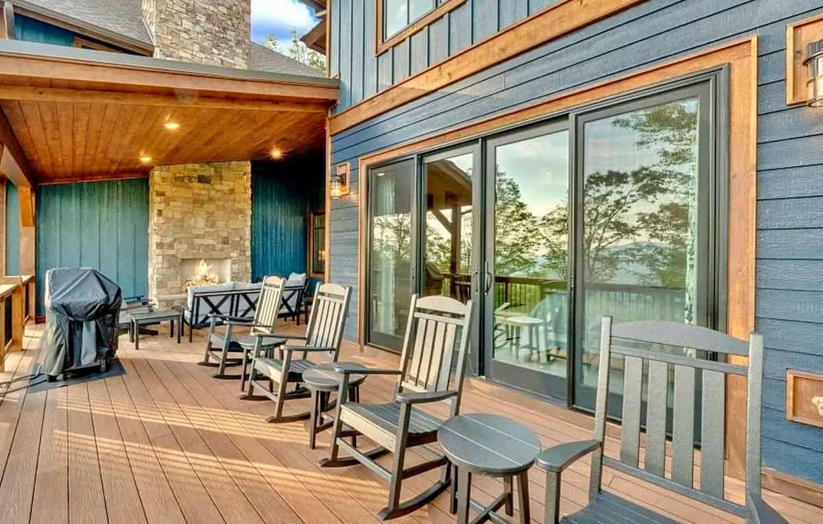 Covered deck with gray rocking chairs, outdoor fireplace, and blue board-and-batten siding