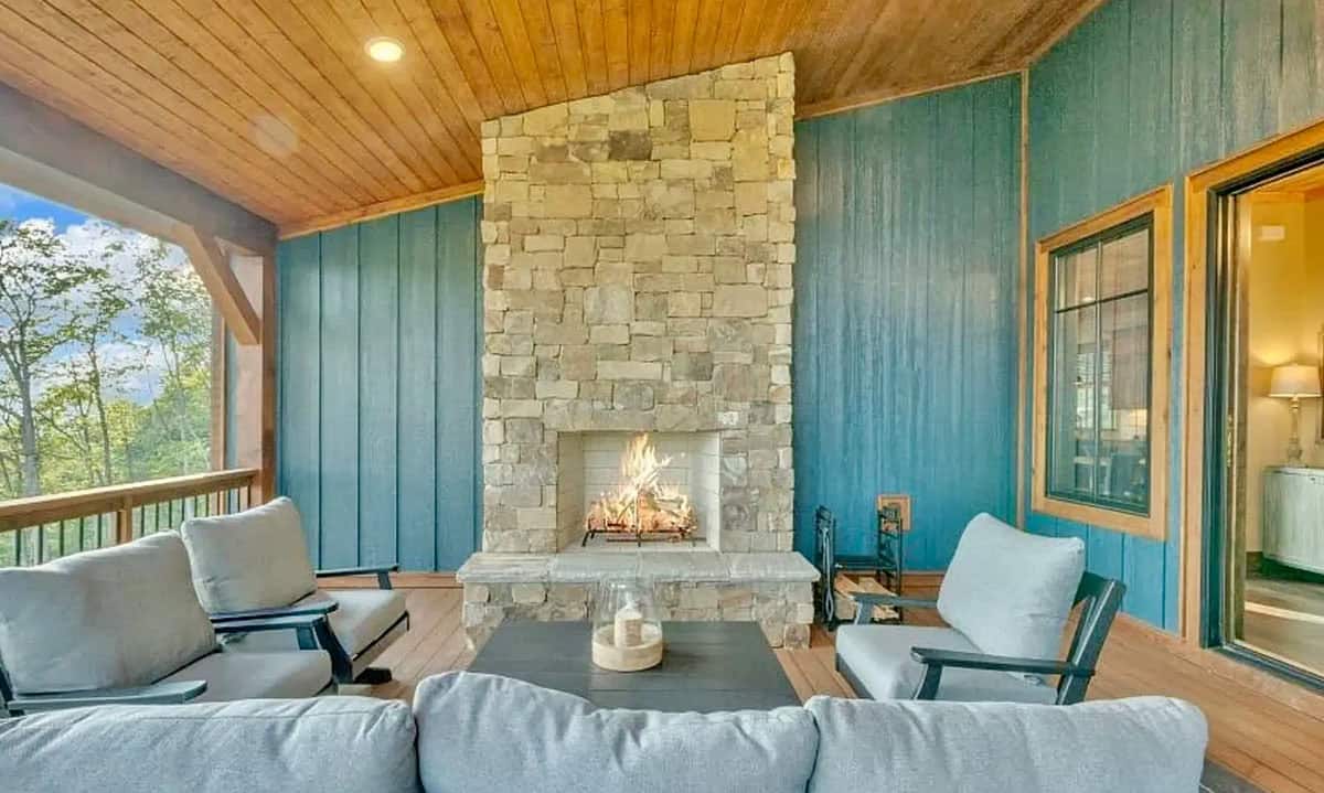 Screened porch with stone fireplace, gray outdoor furniture, and forest views
