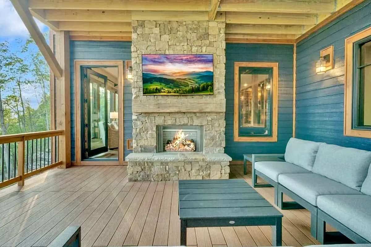 Lower covered porch with stone fireplace, TV, and modern gray sectional